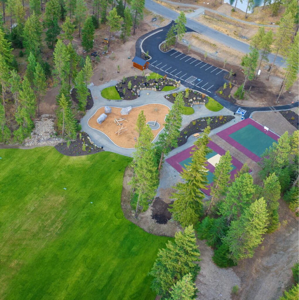 Aerial view of the scenic Suncadia Resort, featuring a vibrant park with a playground, a basketball court, and ample parking, all surrounded by lush greenery. Nearby Cle Elum restaurants offer delicious dining options to complement your day of outdoor fun.