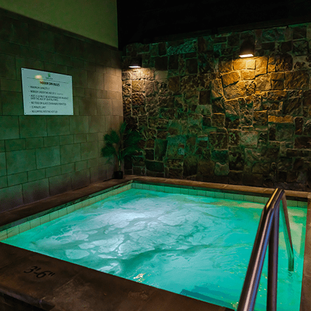 Indoor spa pool with bubbling water, surrounded by tiled walls and stone accents, with a metal handrail and a sign displayed on the wall.