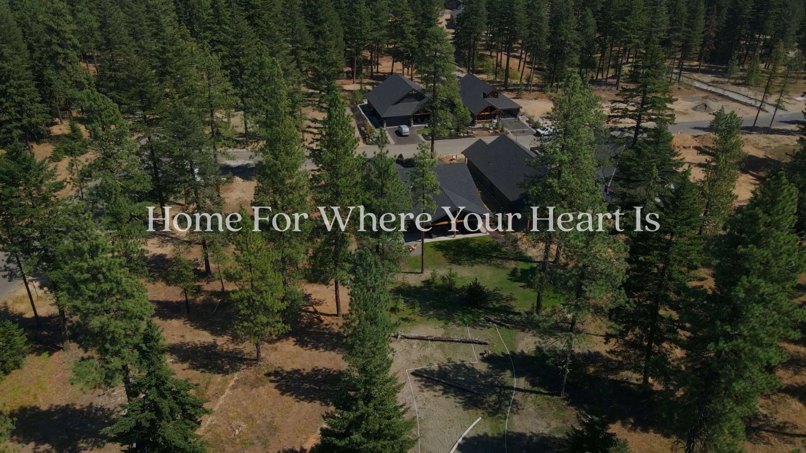Aerial view of houses among tall pine trees with the text “Home For Where Your Heart Is” overlaid in the center.