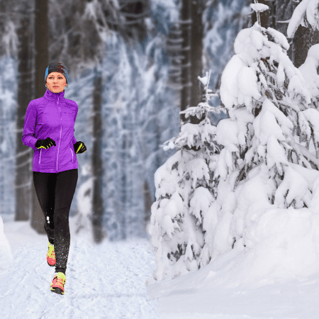 A person in a purple jacket jogs on a snowy trail through a forest with snow-covered trees.