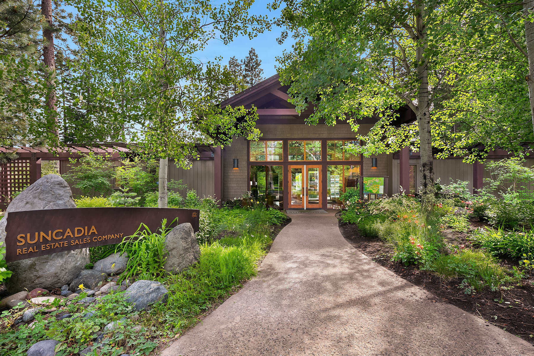 A modern building surrounded by lush greenery with a sign reading “Suncadia Real Estate Sales Company” near the entrance.
